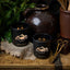Two lit black candles with 'Black Hills Candle' branding on a rustic wooden surface with decorative elements.