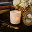 Candle with 'Hills' logo on a dark surface with books, flowers, and a picture frame.