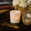 Candle with 'Canter Hills' branding on a dark surface with books, flowers, and a picture frame.