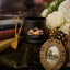 Black candle with 'Black Hills Candle' logo on a decorative surface with books and flowers.
