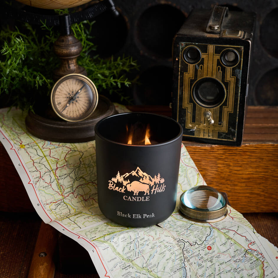 Black candle with 'Black Hills Candle' branding on a map with vintage items around