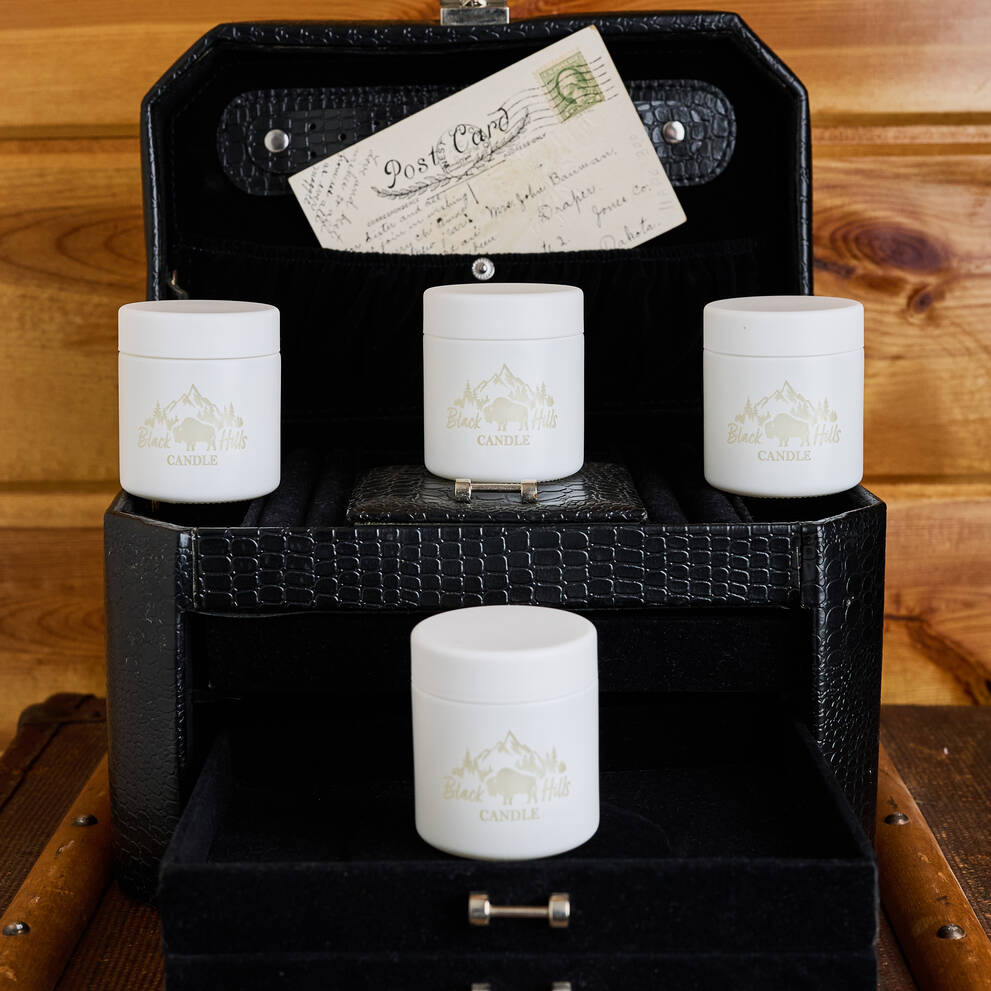 Set of white candles with a brand logo in a black decorative box on a wooden surface