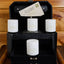 Set of white candles with a brand logo in a black decorative box on a wooden surface