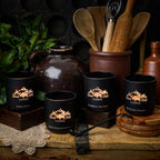 Black mugs with 'Black Hills Candle' logo on a rustic wooden surface with kitchen utensils and a jar.