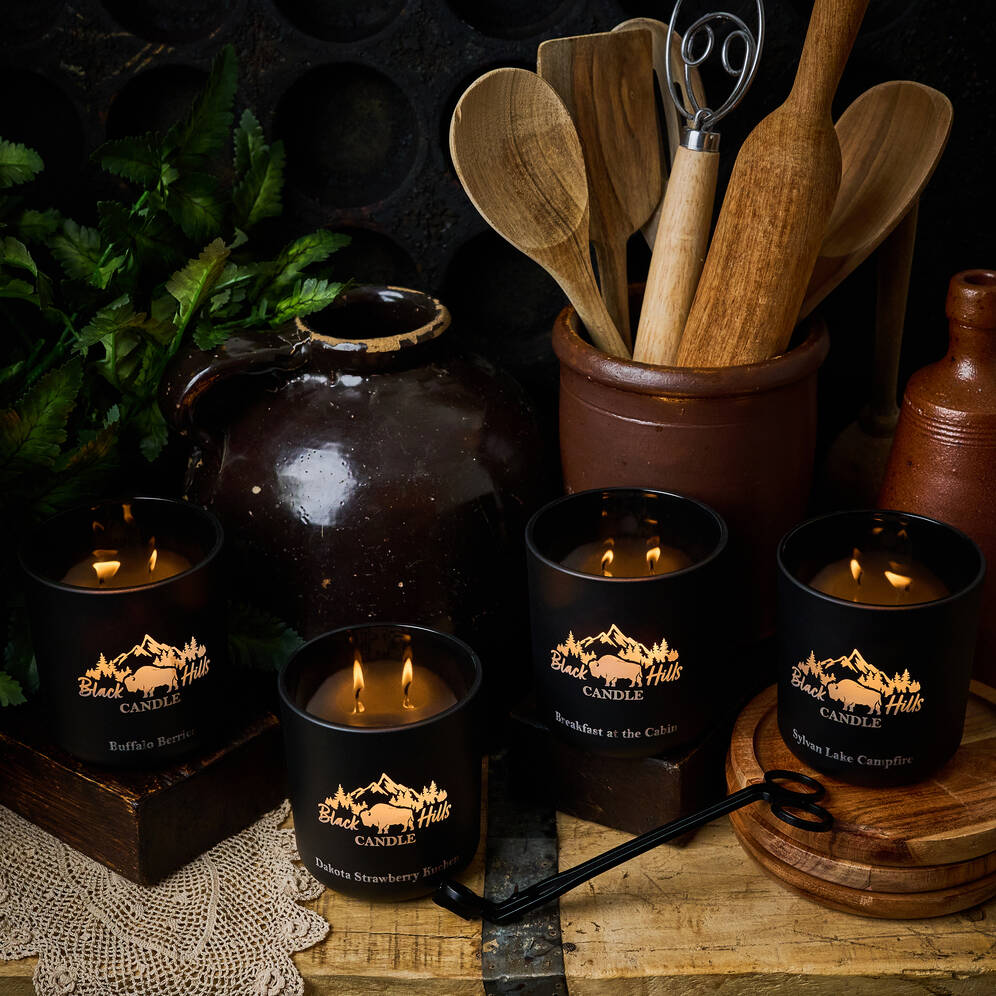 Black candles with mountain design on a rustic wooden surface with kitchen utensils and a pot.