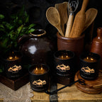 Black candles with mountain design on a rustic wooden surface with kitchen utensils and a pot.