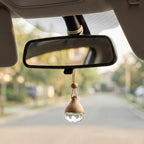 Wooden car hanging ornament with a clear droplet attached to a car's rearview mirror.