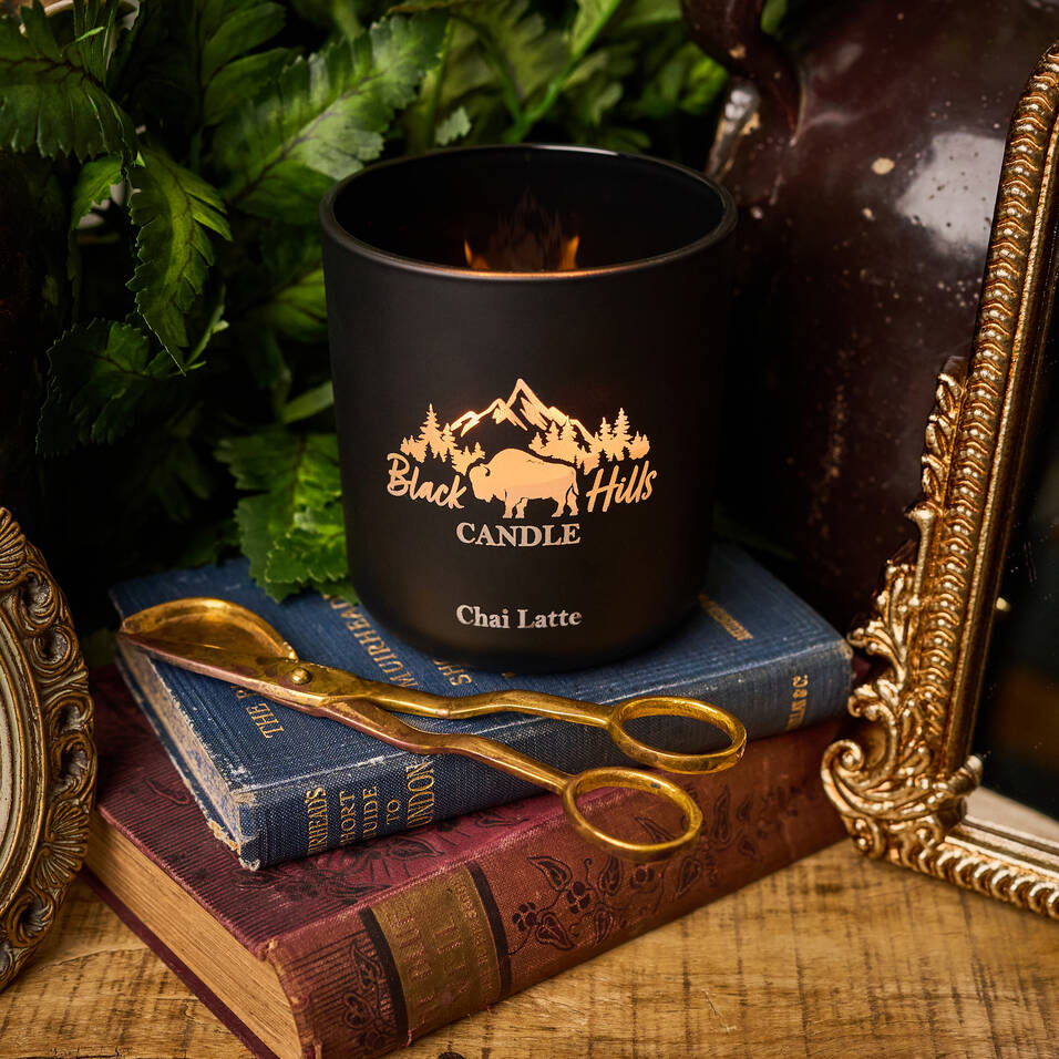 Black candle labeled 'Black Hills Candle' on a stack of books with decorative items.