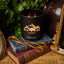 Black candle with 'Black Hills Candle Coffee Cabin' branding on a stack of books with gold scissors.