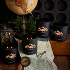Black candles with 'Black Hills Candle' branding on a map with a vintage camera and globe in the background.