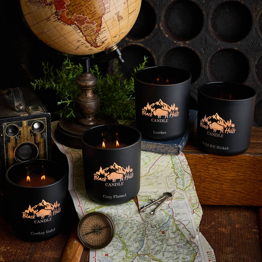 Black candles with 'Black Hills Candle' branding on a map with a vintage camera and globe in the background.