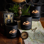 Black candles with 'Black Hills Candle' branding on a map with compass and vintage camera.