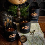 Black candles with 'Black Hills Candle' branding on a map with a vintage camera and globe.