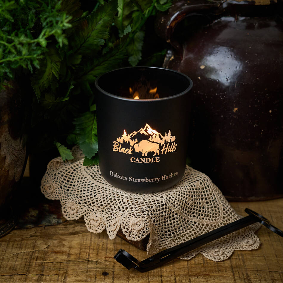 Black candle with 'Black Hills Candle' logo on a lace doily with a rustic background