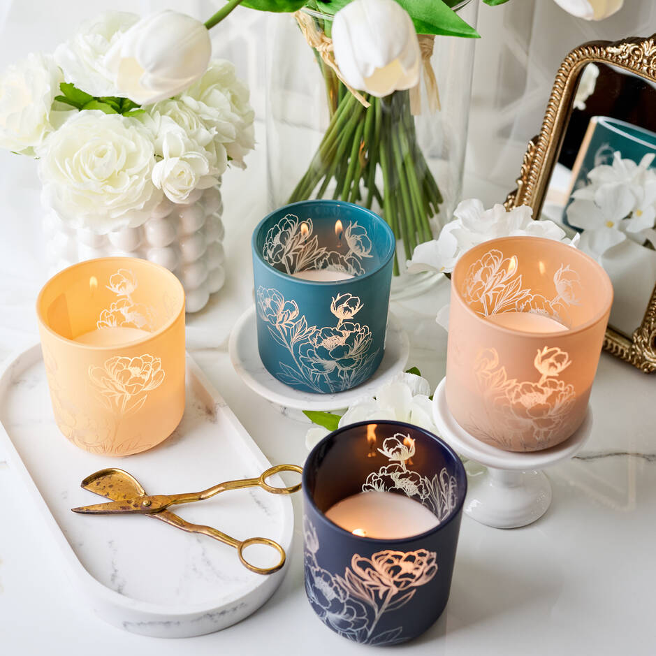 Decorative candles with floral designs on a marble surface with flowers and a mirror in the background. Main image