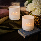 Two lit candles on books with decorative elements including flowers and books in the background.