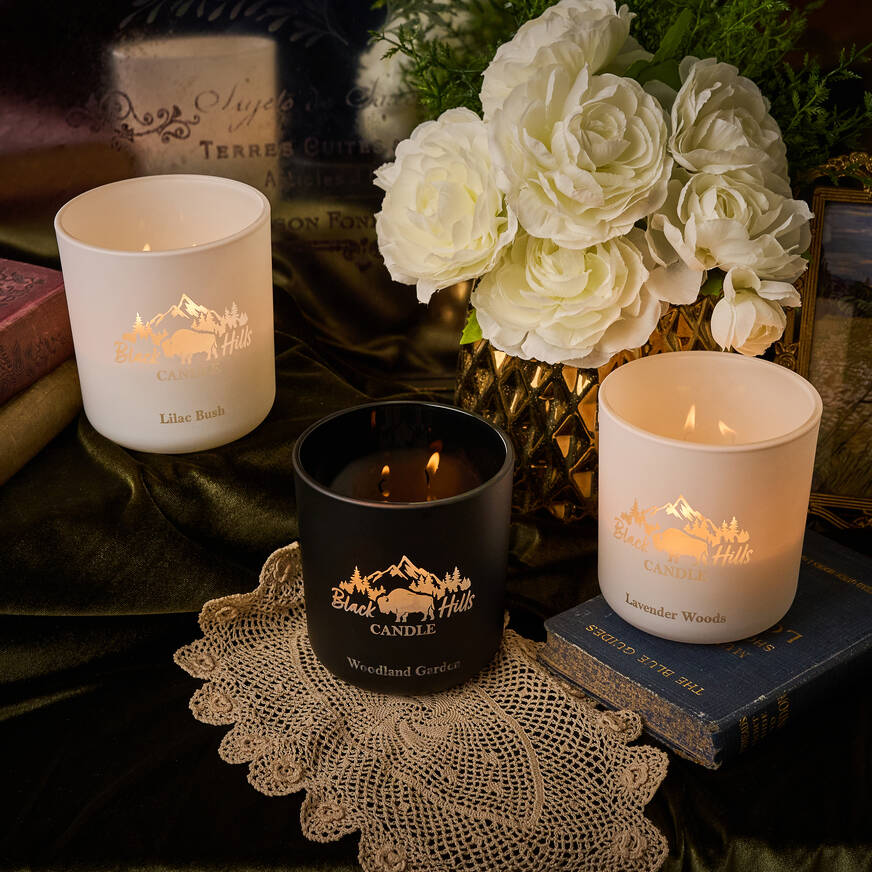 Three candles with different scents on a table with flowers and books in the background