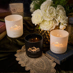Three candles with different scents on a table with flowers and books in the background