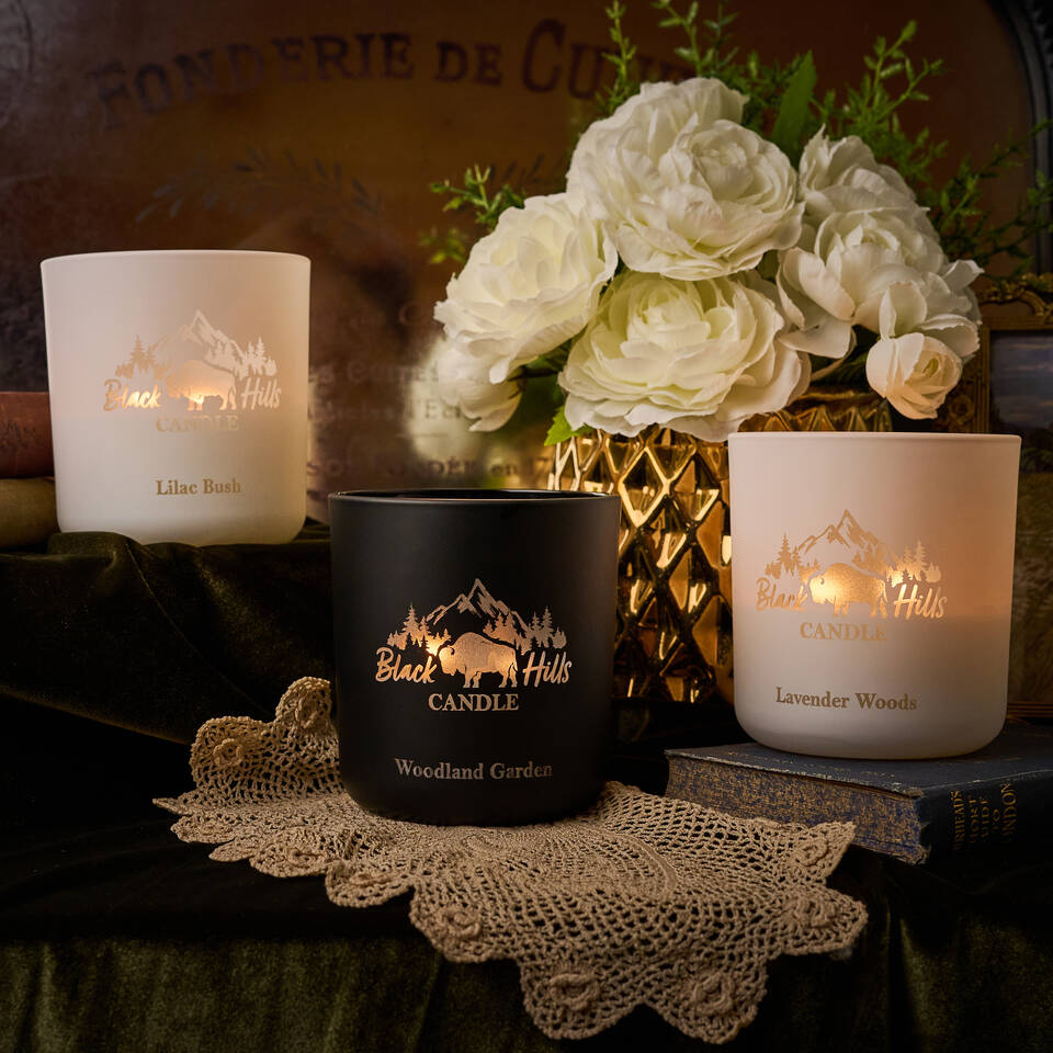 Three candles with decorative labels on a table with flowers and doilies.