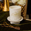 White candle with 'Black Hills Candle' branding on a decorative surface with gold accents and flowers.