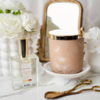 Perfume bottle and decorative candle on a marble surface with flowers and a mirror in the background.