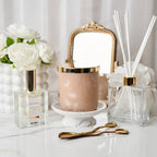 Decorative items including a candle, diffuser, and flowers on a white surface with a mirror in the background.