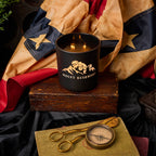 Candle with Mount Rushmore design on a wooden block, surrounded by vintage items like scissors and a compass, with a flag in the background.