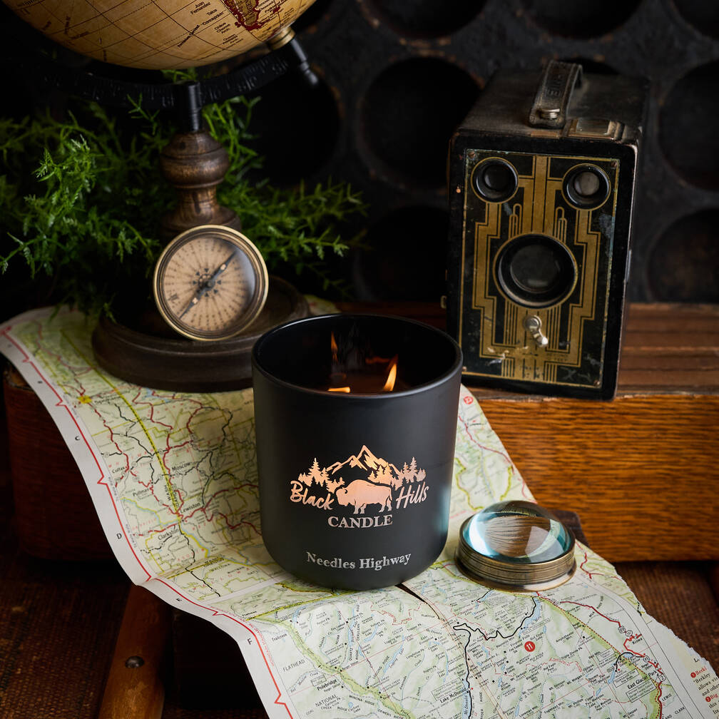 Black candle with 'Black Hills Candle' logo on a map with vintage items around Main image