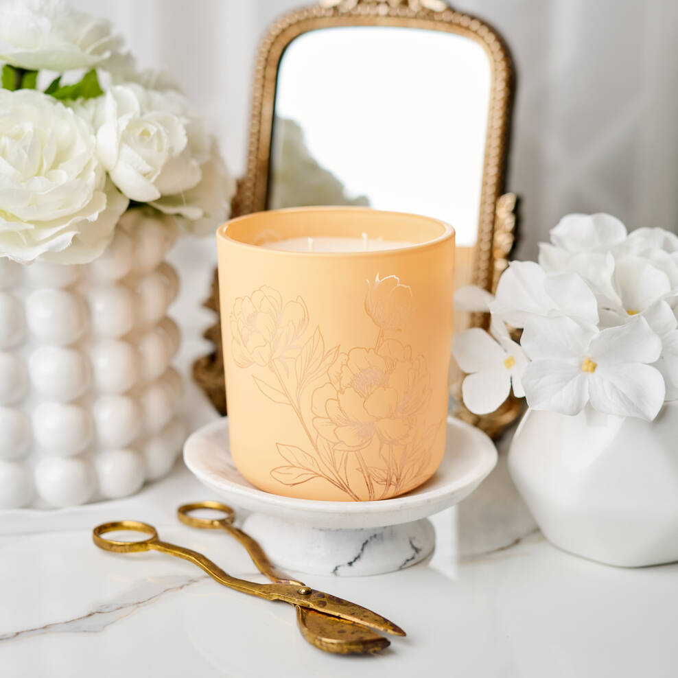 Decorative candle on a marble surface with white flowers and a mirror in the background
