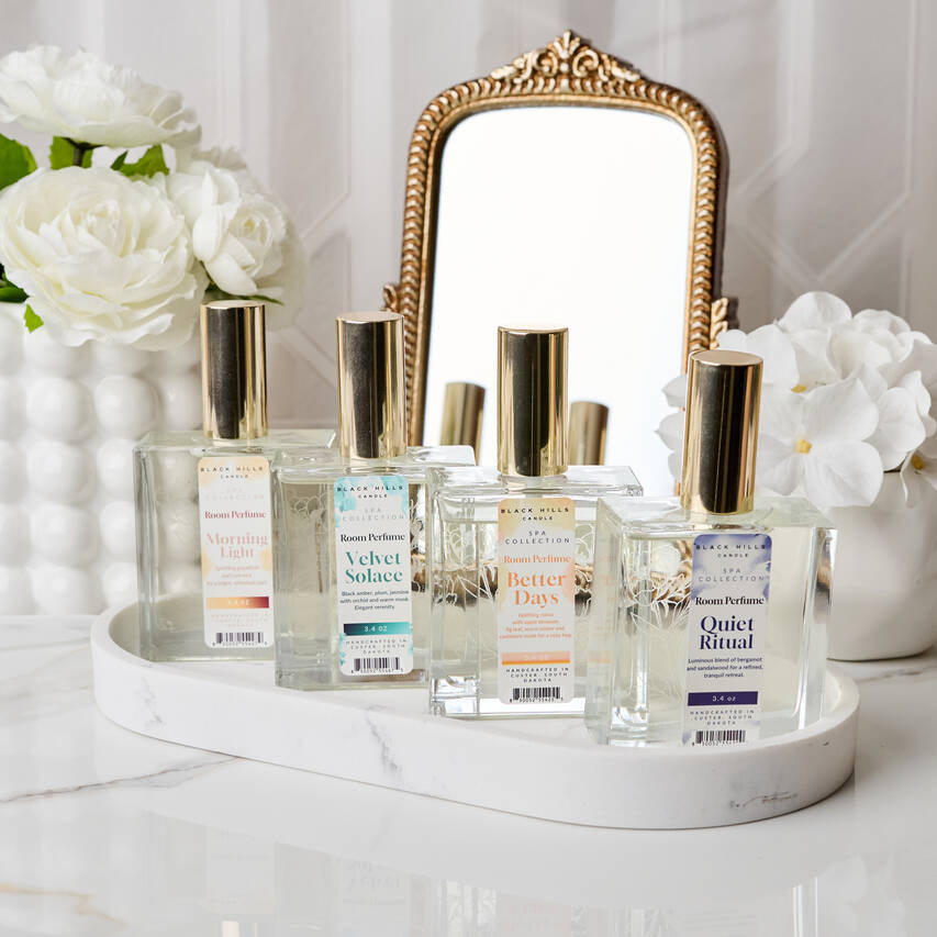 Collection of perfume bottles on a tray with a decorative mirror and flowers in the background