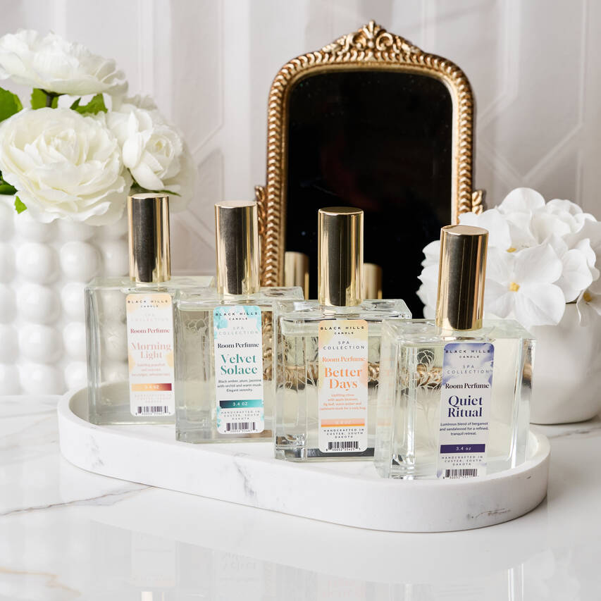 Collection of perfume bottles on a white surface with flowers and a mirror in the background Main image