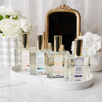 Collection of perfume bottles on a white surface with flowers and a mirror in the background