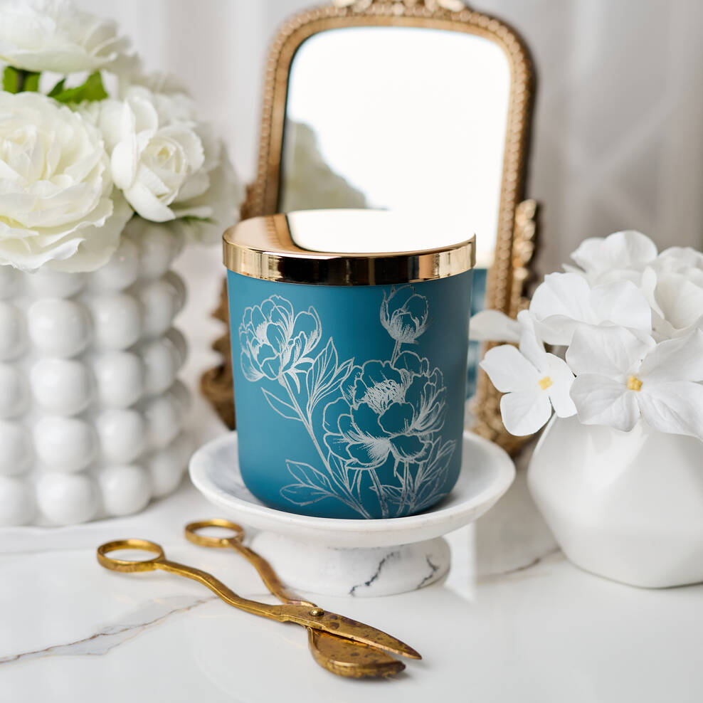 Blue candle with floral design on a white surface with decorative items