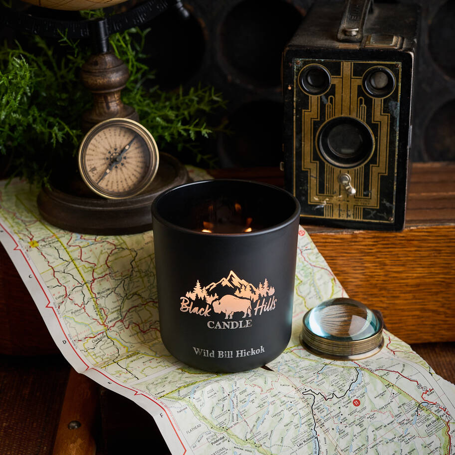 Black candle with 'Black Hills Candle' logo on a map with vintage items