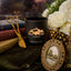 Black candle with 'Black Hills Candle' logo on a surface with decorative items like a gold frame and white flowers.