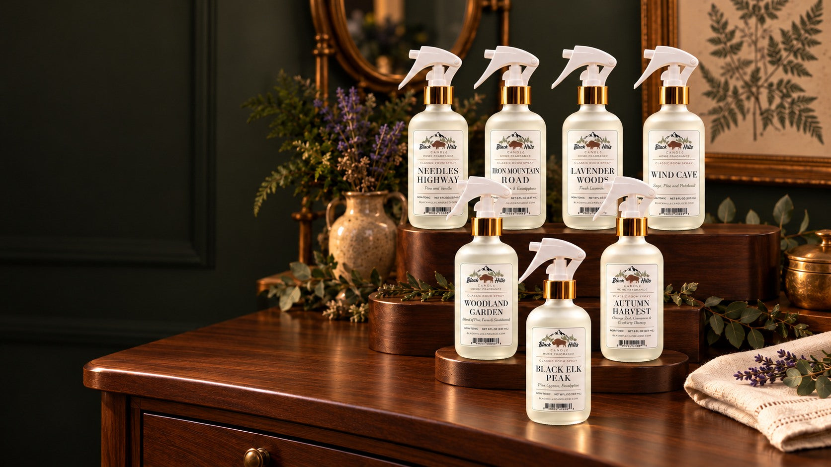 Black Hills room sprays in frosted glass bottles with white trigger sprayers and gold collars, together in a warm country lodge setting